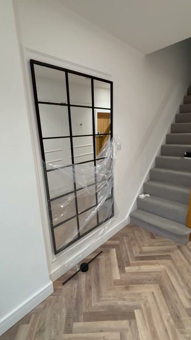 Hallway with herringbone flooring, stairs and a black-framed mirror